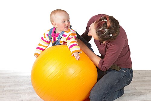 A lady holding a baby on an exercise ball.