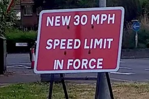 A picture with a sign that says "New 30MPH Speed limit in force"