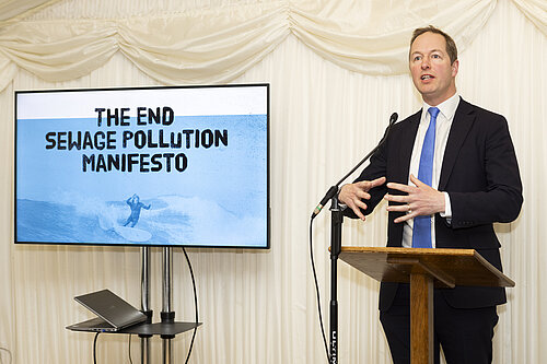 Richard Foord standing at a podium next to a presentation slide reading "The End Sewage Pollution Manifesto"