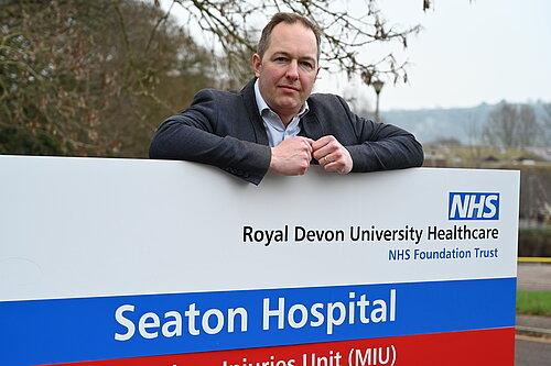 Richard Foord standing behind the sign for Seaton Hospital